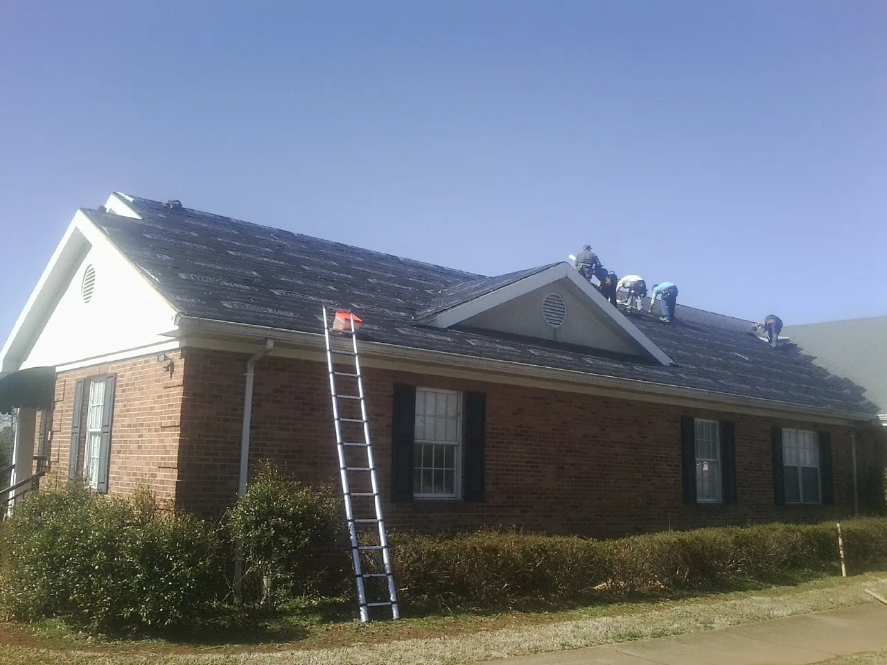 Crew tearing shingles off a brick ranch roof with a ladder set — Emergency Roof Repair work by our crew in South Hadley