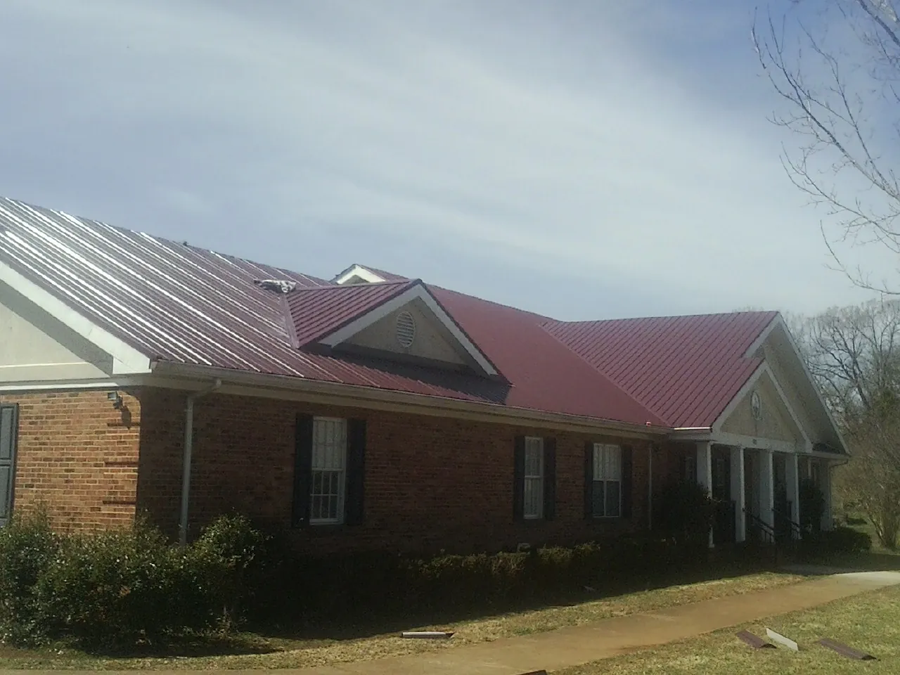 Red metal roof with gabled entries on a long brick building, from a Hail Damage Roof Repair job in South Hadley