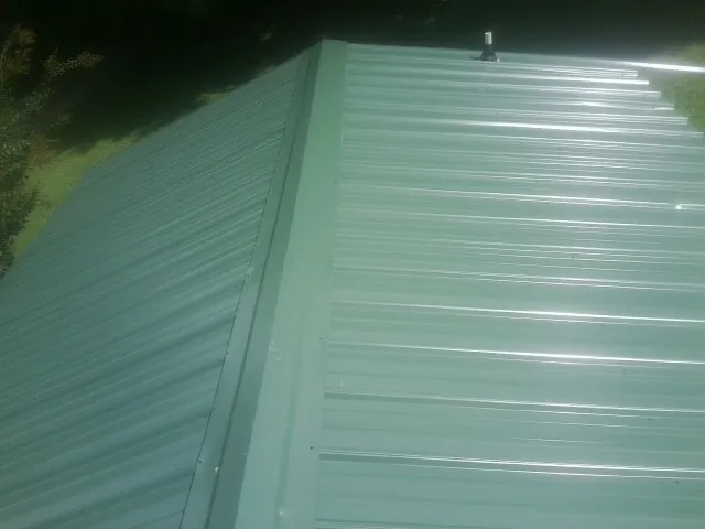 New green metal panels meeting at the ridge of a roof — Flat Roof Repair work by our crew in South Hadley
