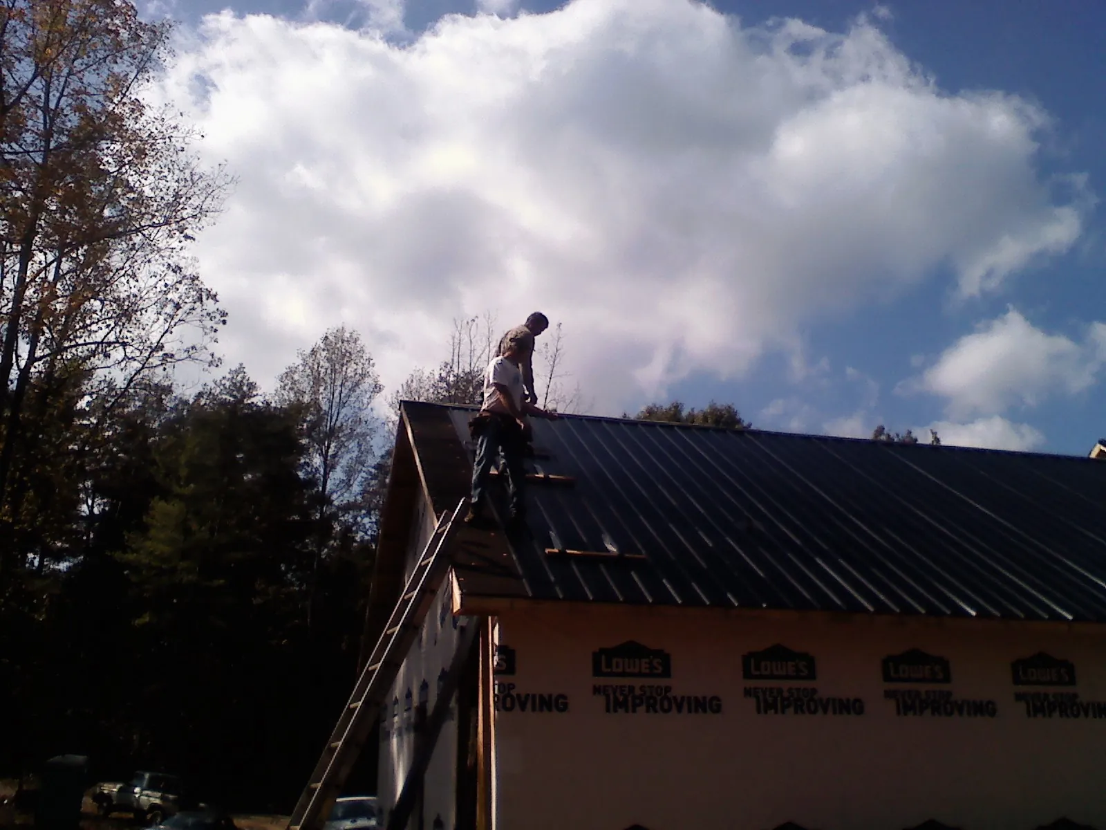 Roofer fastening dark metal panels high against a cloudy sky, from a Roof Inspection job in South Hadley