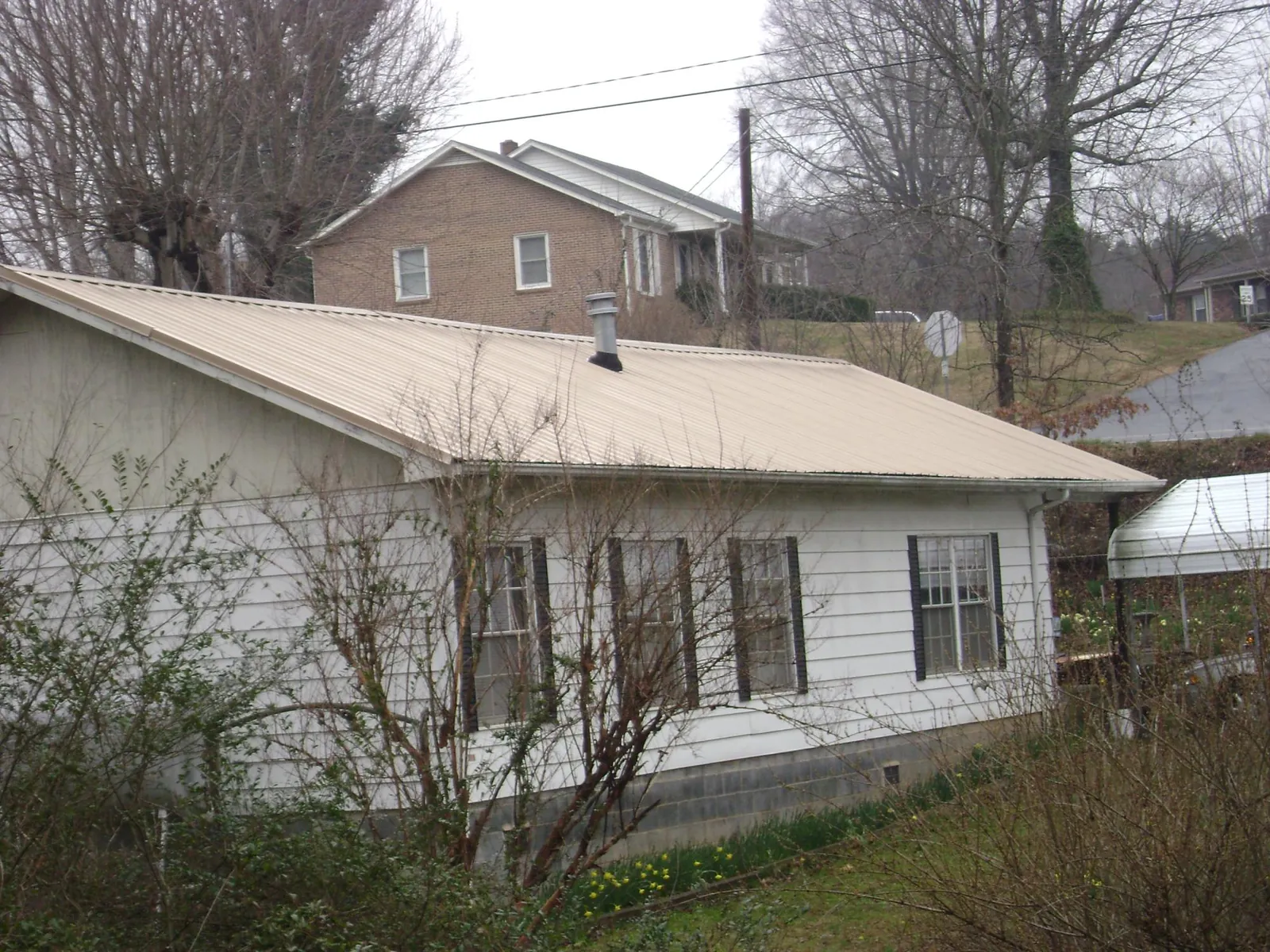Tan metal roof on a white sided house set into a hillside — Commercial Roofing by Roofing Brothers in South Hadley
